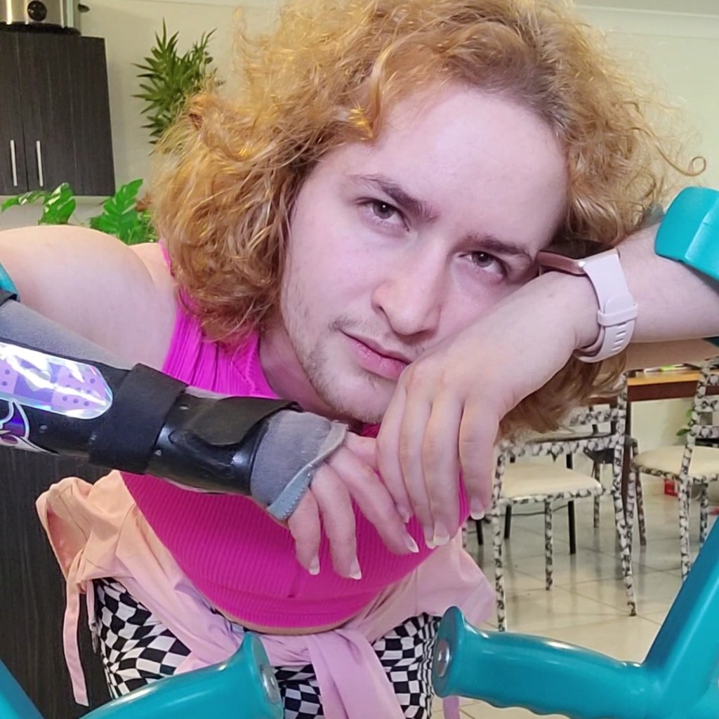 Myself, a white man with shoulder length blonde hair, leaning on my teal forearm crutches.